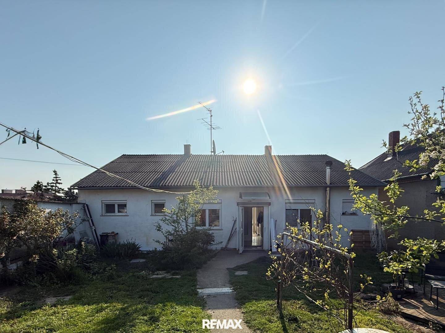 Rückansicht des Hauses mit mehreren Fenstern und Zugang zum Garten unter strahlendem Himmel.