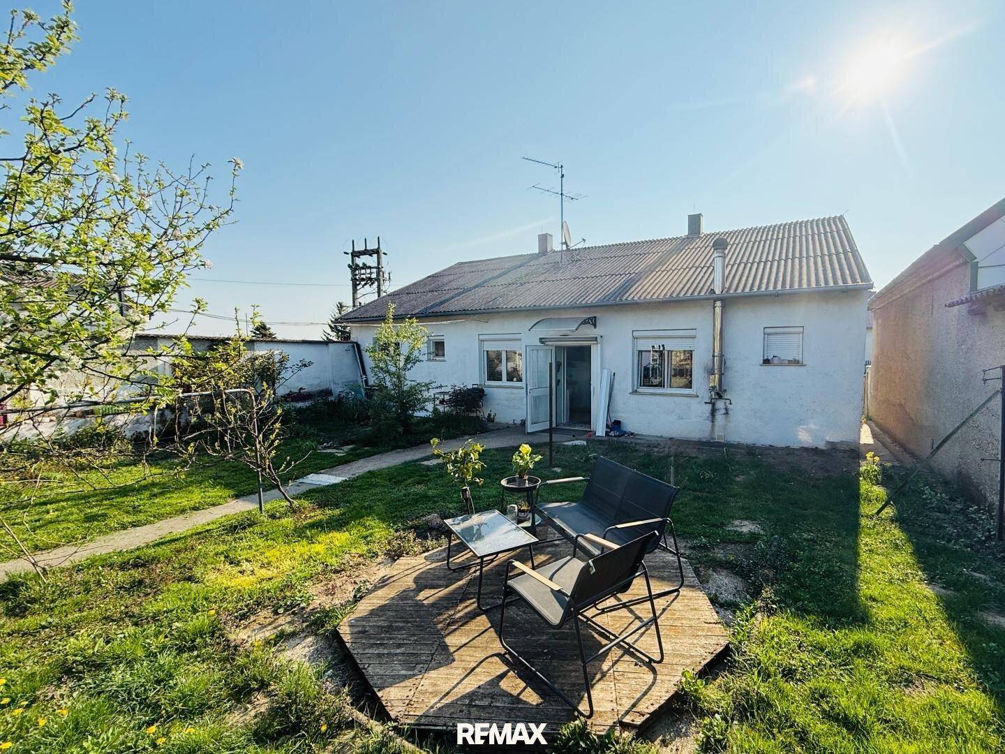 Kleiner Gartenbereich hinter dem Haus mit Sitzgelegenheit und viel Grünfläche unter strahlendem Himmel.