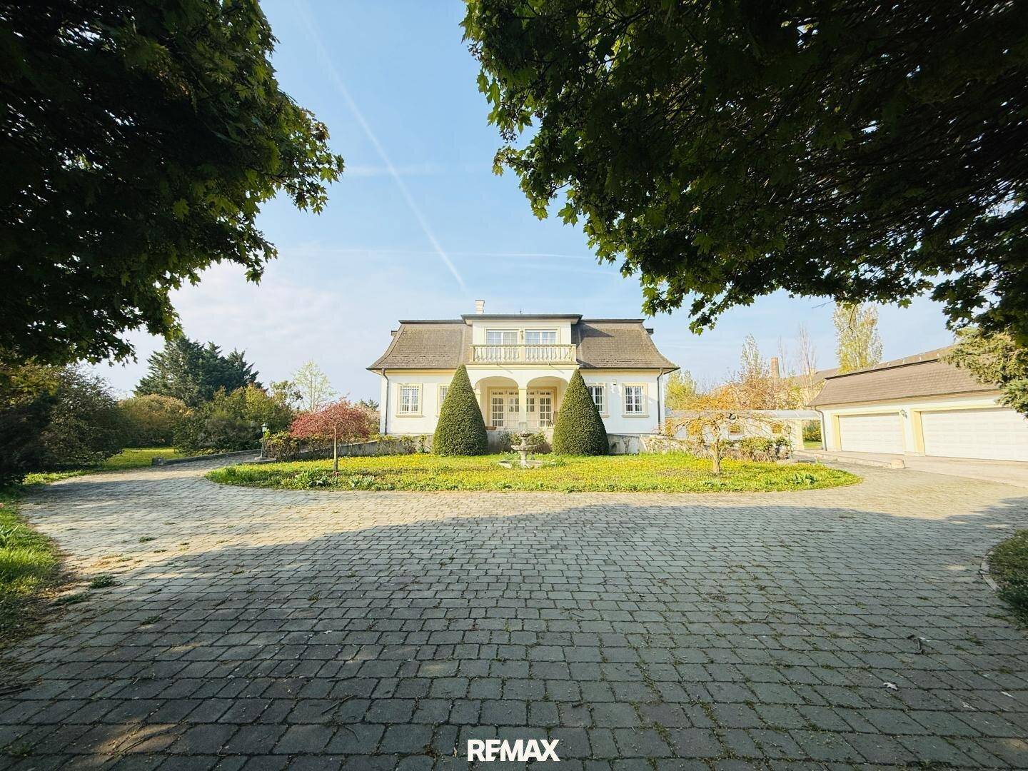 Weitläufige Auffahrt aus Kopfsteinpflaster führt zu einer eleganten Villa mit großem Garten und altem Baumbestand.