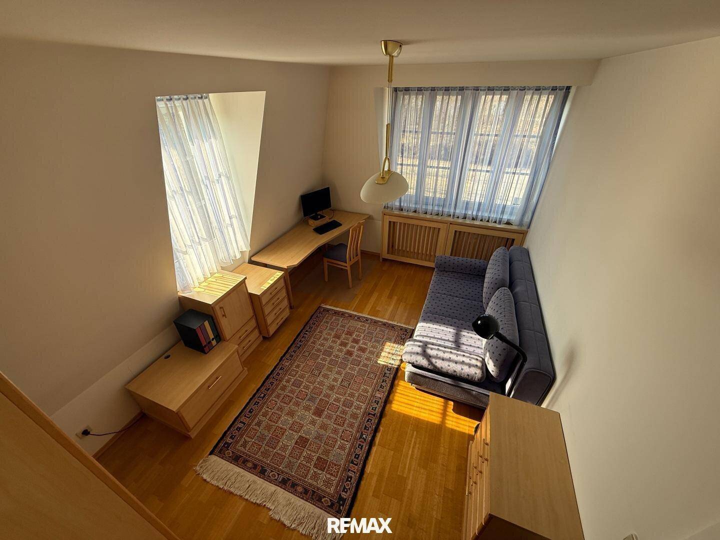 Helles Arbeitszimmer im Dachgeschoss mit Schreibtisch, Sofa und Holzboden.