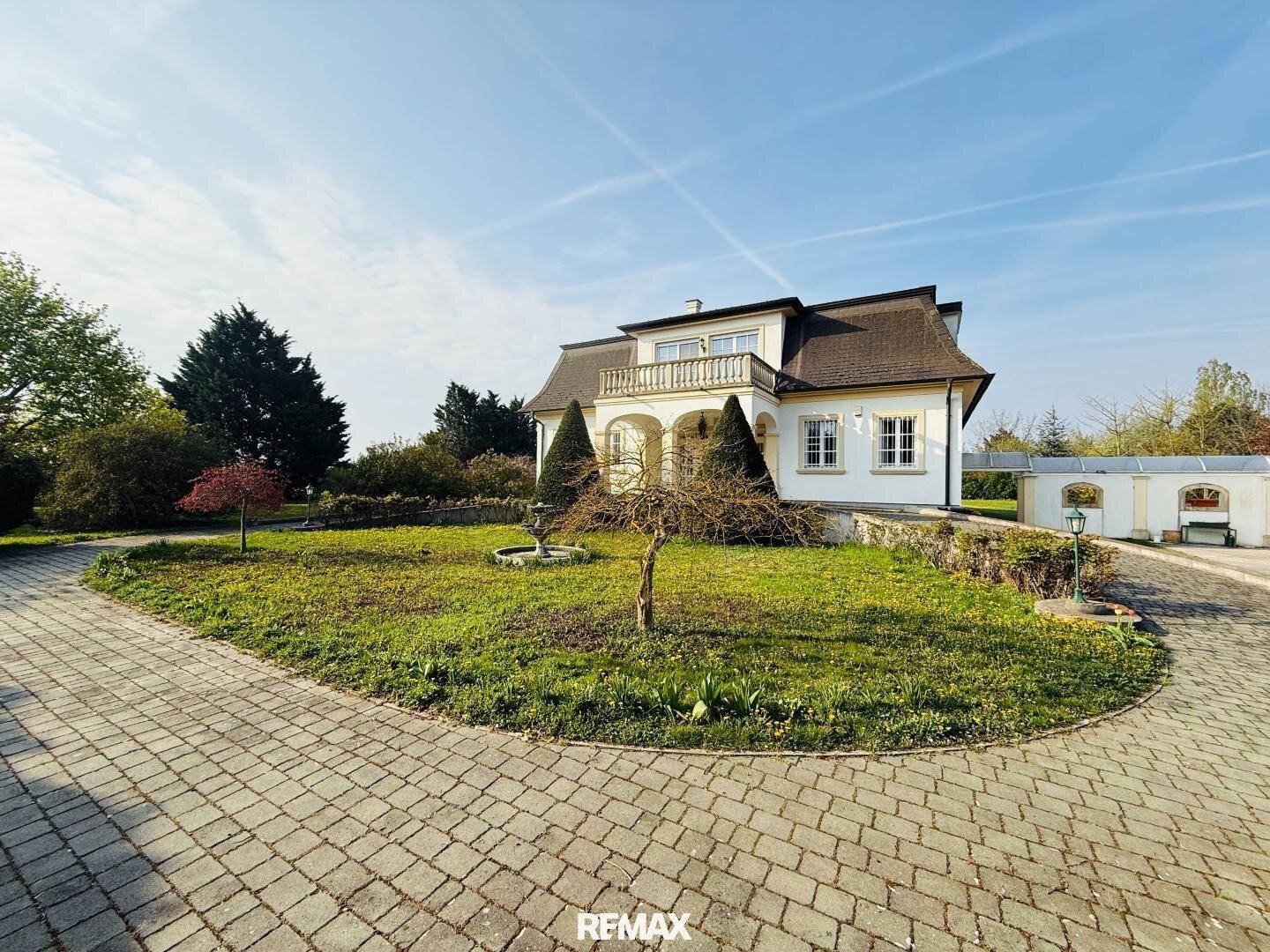 Weitläufige Auffahrt aus Kopfsteinpflaster führt zu einer eleganten Villa mit großem Garten und altem Baumbestand.