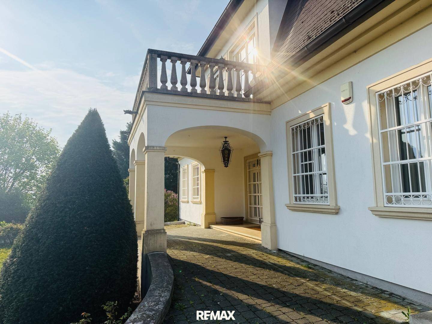 Überdachter Eingangsbereich der Villa mit klassischen Säulen und einem Balkon im Obergeschoss.