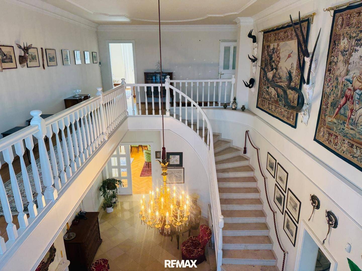 Elegante geschwungene Treppe in einer hohen Eingangshalle mit Wandteppichen und Jagdtrophäen.