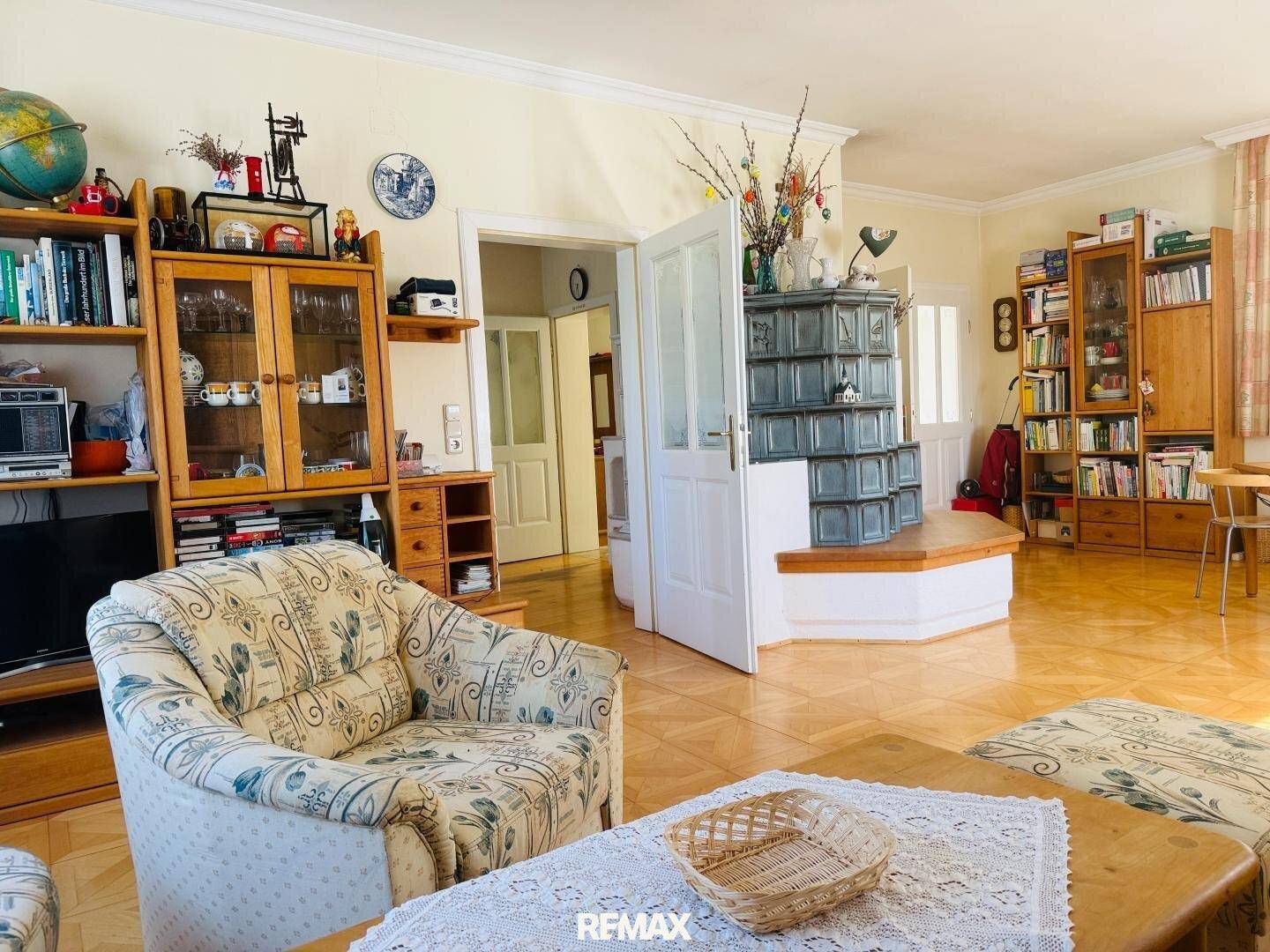 Geräumiges Wohnzimmer mit Kachelofen, Parkettboden und traditionellen Möbeln.