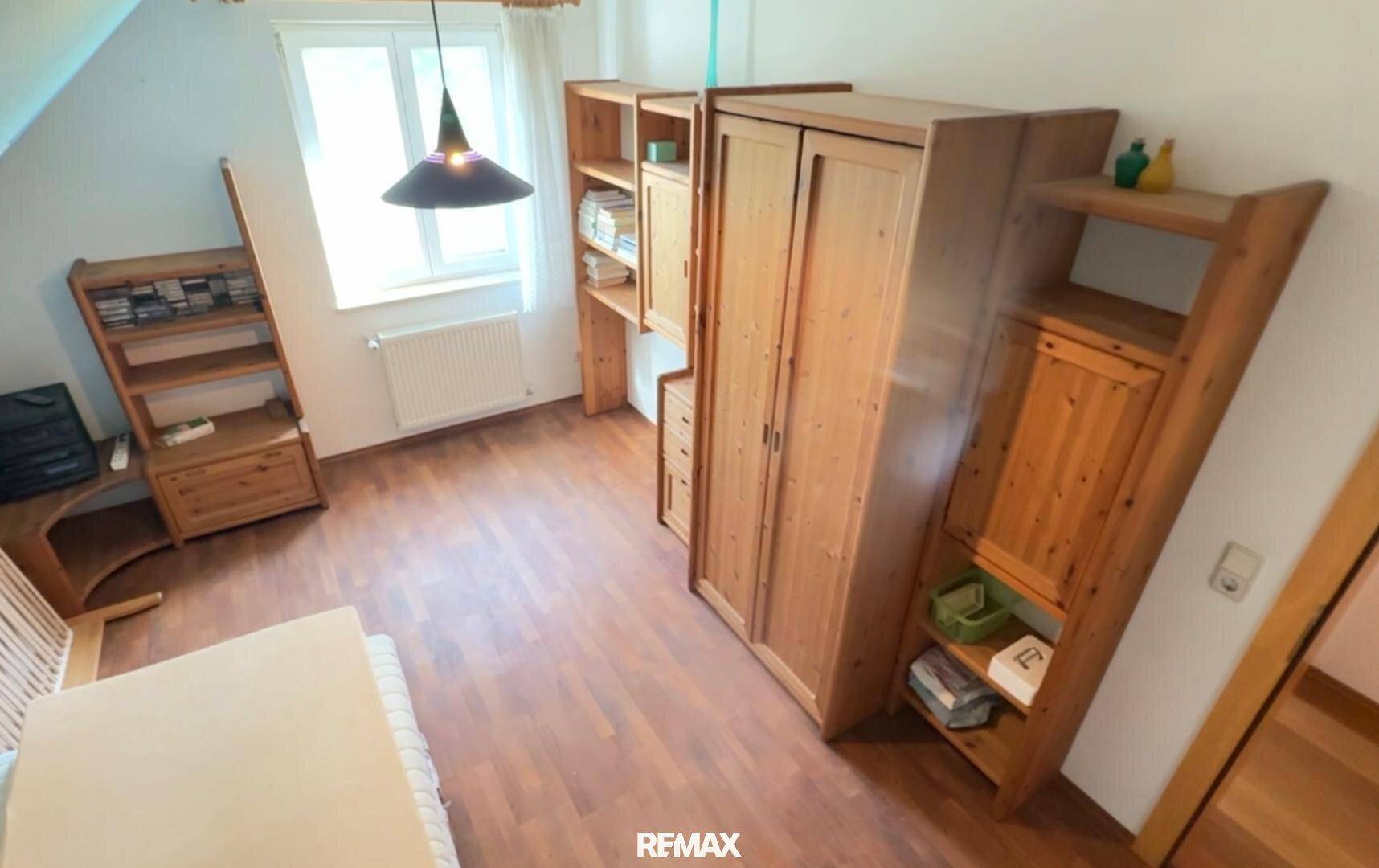 Schlafzimmer mit Holzboden, Holzmöbeln und einem Fenster, das viel Licht hereinlässt.