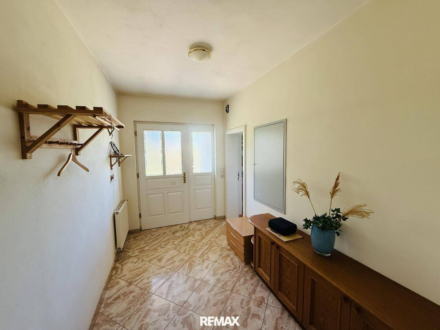 Heller Eingangsbereich mit gefliestem Boden, Garderobe und Holzkommode.