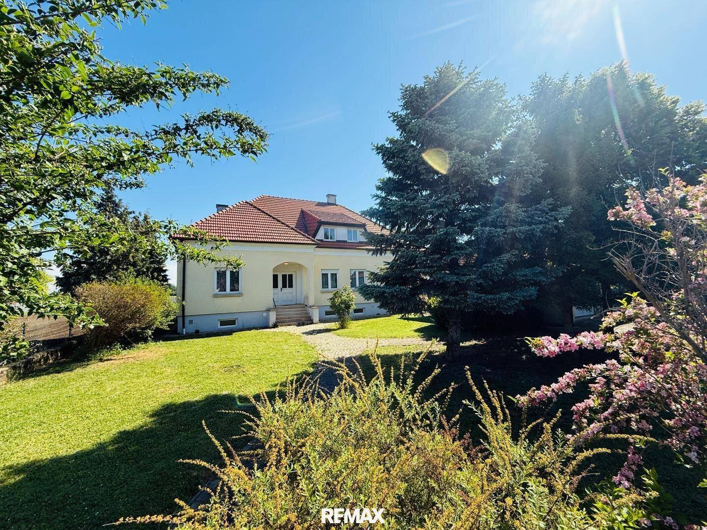 Charmantes Einfamilienhaus mit rotem Ziegeldach und heller Fassade, umgeben von einem großen Garten.