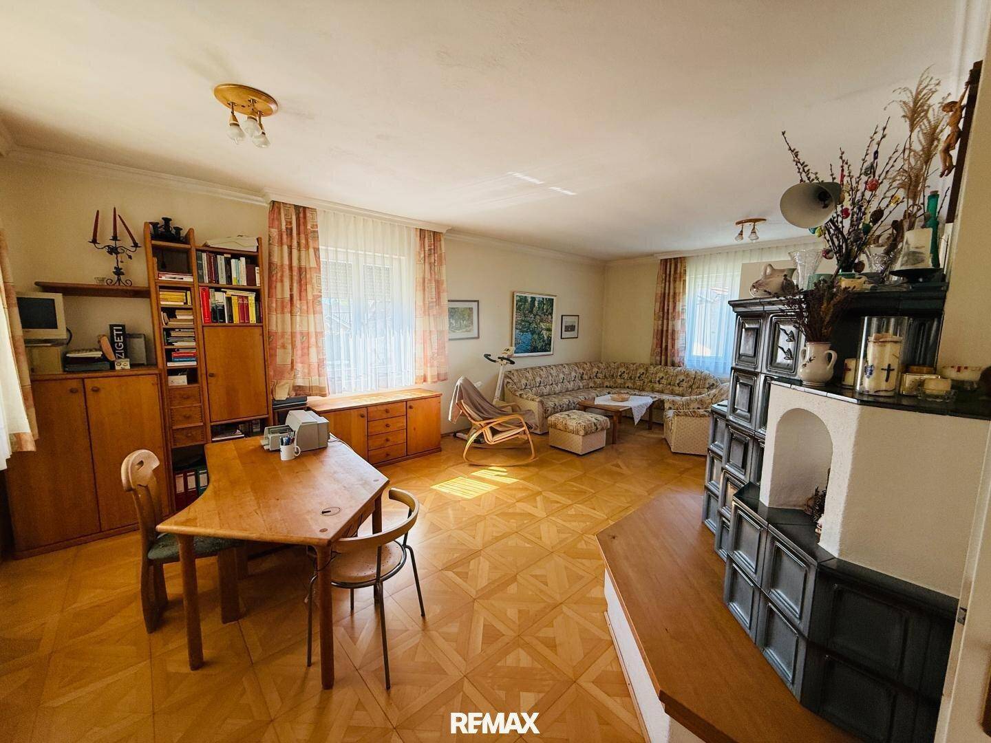 Großes Wohnzimmer mit Kachelofen, Esstisch und Blick in den Garten.