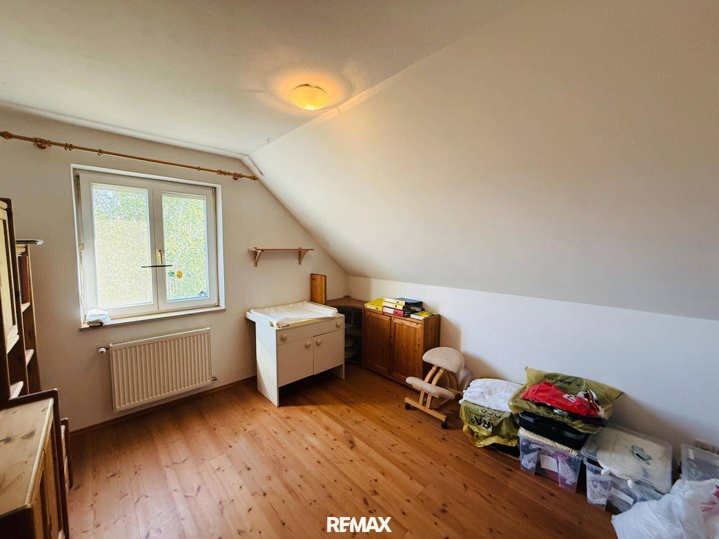 Dachschrägenzimmer mit Holzboden, Fenster und einfacher Einrichtung, ideal als Kinderzimmer.