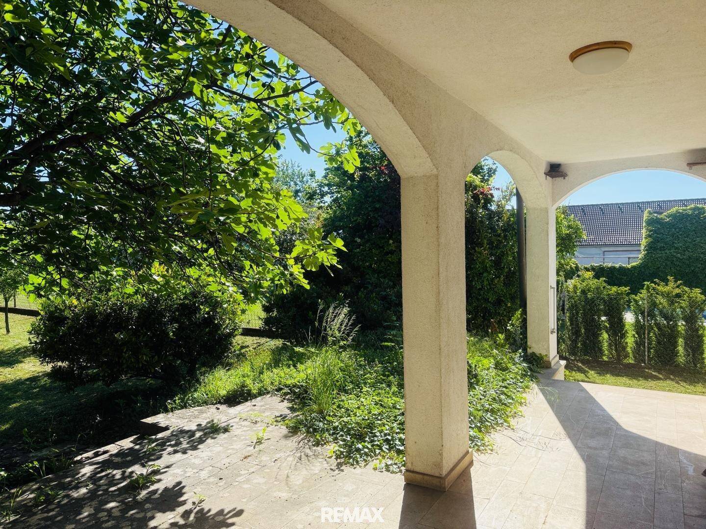 Überdachte Terrasse mit Säulen und Blick auf den grünen Gartenbereich.