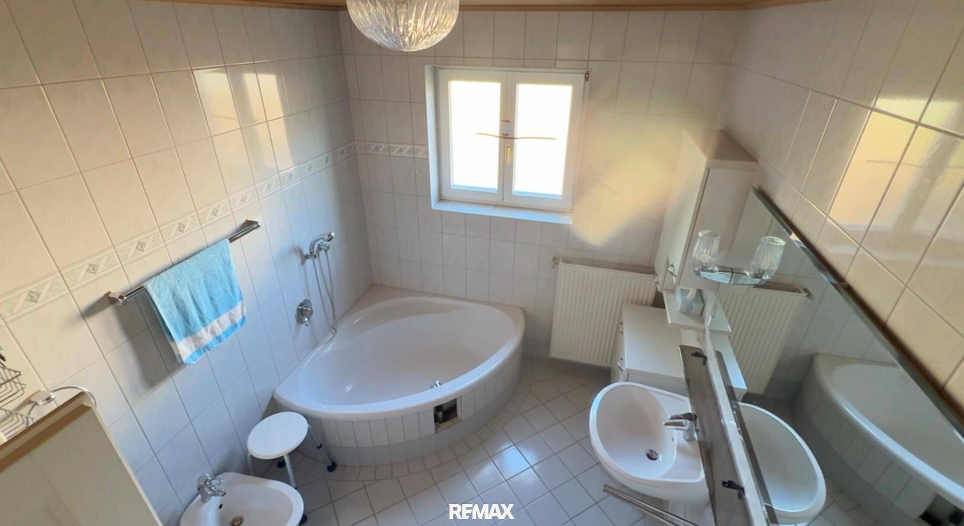 Badezimmer mit Eckbadewanne, Bidet und Fenster, hell gefliest.