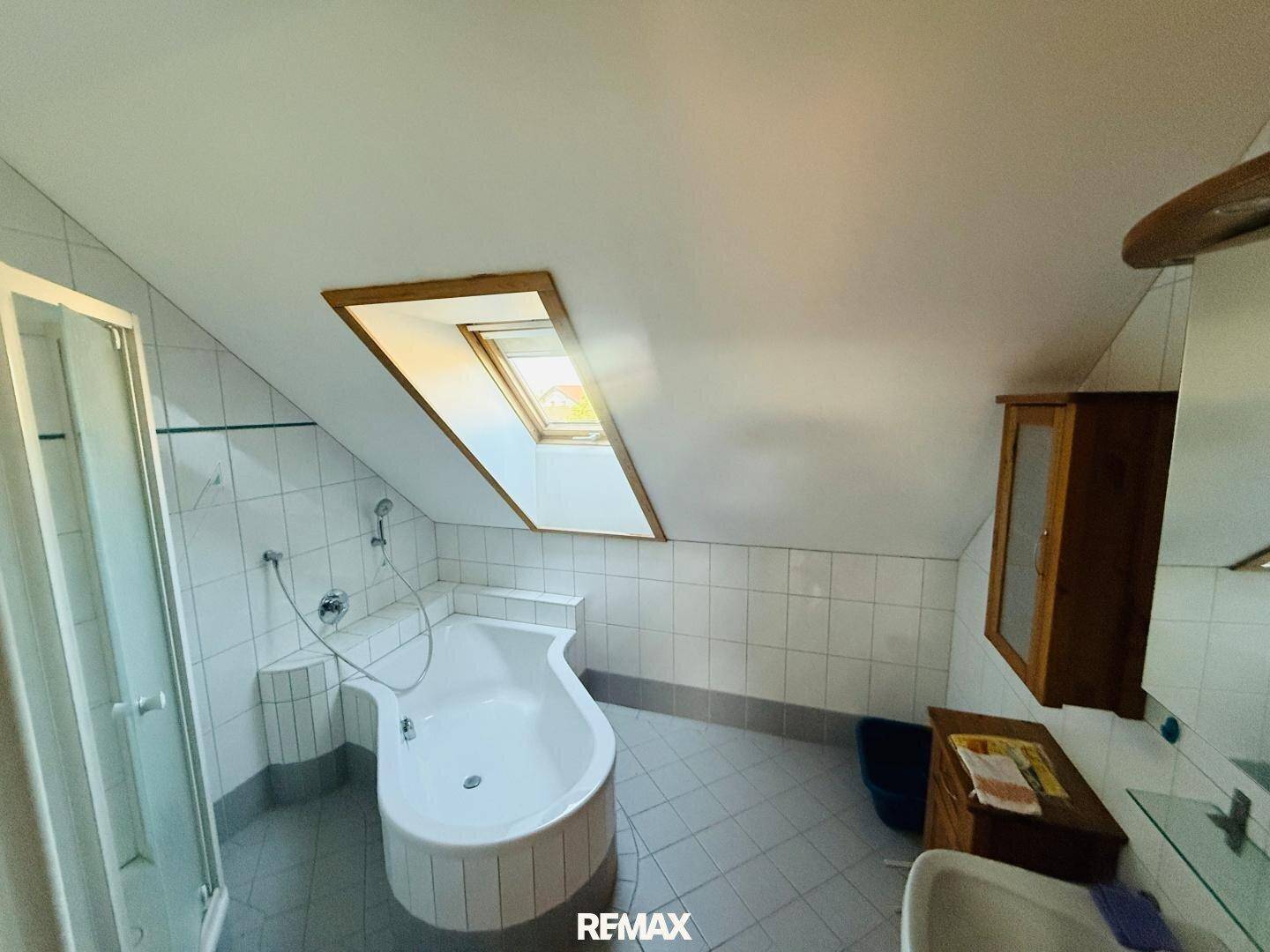 Badezimmer mit Dachfenster, Badewanne und Duschkabine unter einer Dachschräge.