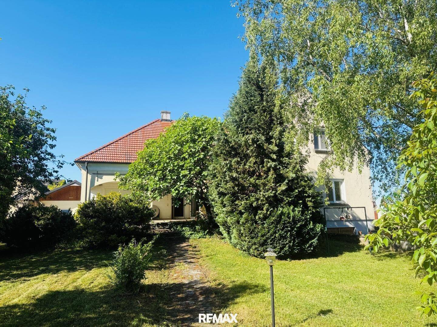 Rückansicht des Hauses, umgeben von hohen Bäumen und üppigem Grün im Gartenbereich.