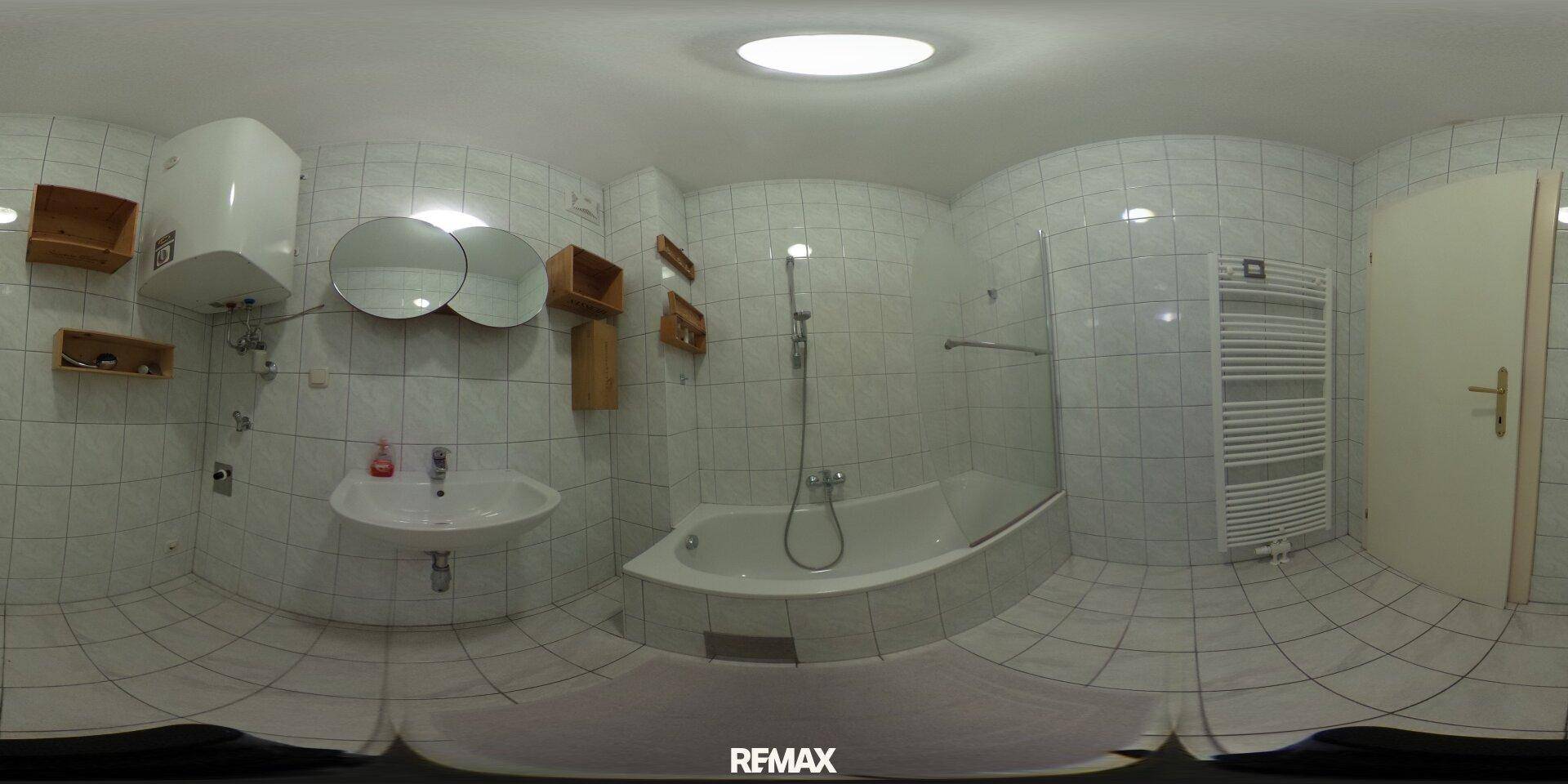 Panoramaansicht des gefliesten Badezimmers mit Badewanne, Duschfunktion und Heizkörper.