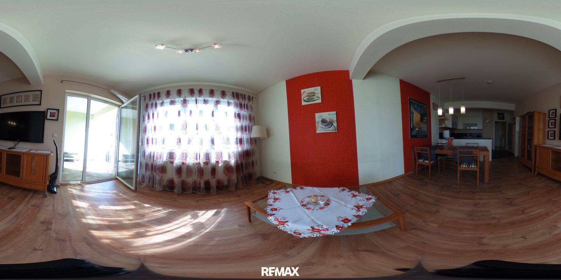 Panoramaansicht des hellen Wohnzimmers mit Holzboden und Zugang zum Balkon.