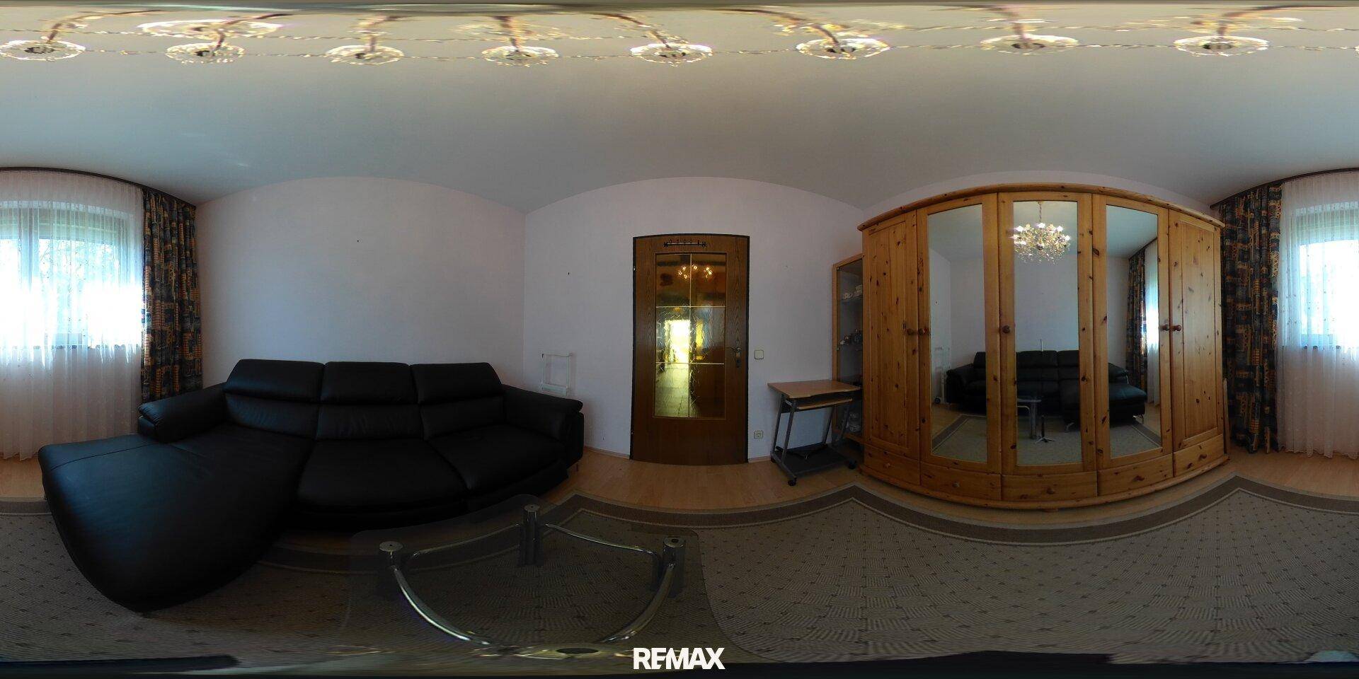 Wohnzimmer mit großem schwarzem Sofa, Glastisch und einem eleganten Holzschrank mit Spiegeln.
