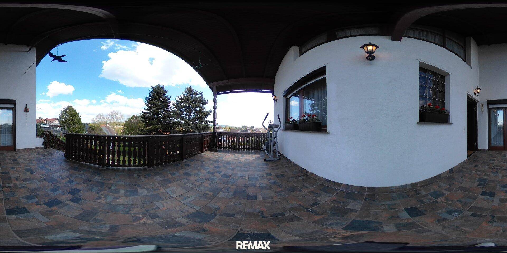 Große überdachte Terrasse mit Fliesenboden, Balustrade und weitem Blick über die Umgebung.