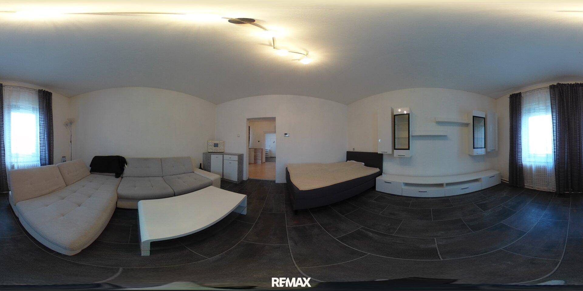 Kombinierter Wohn- und Schlafbereich mit Sofa, Bett und dunklem Fliesenboden.