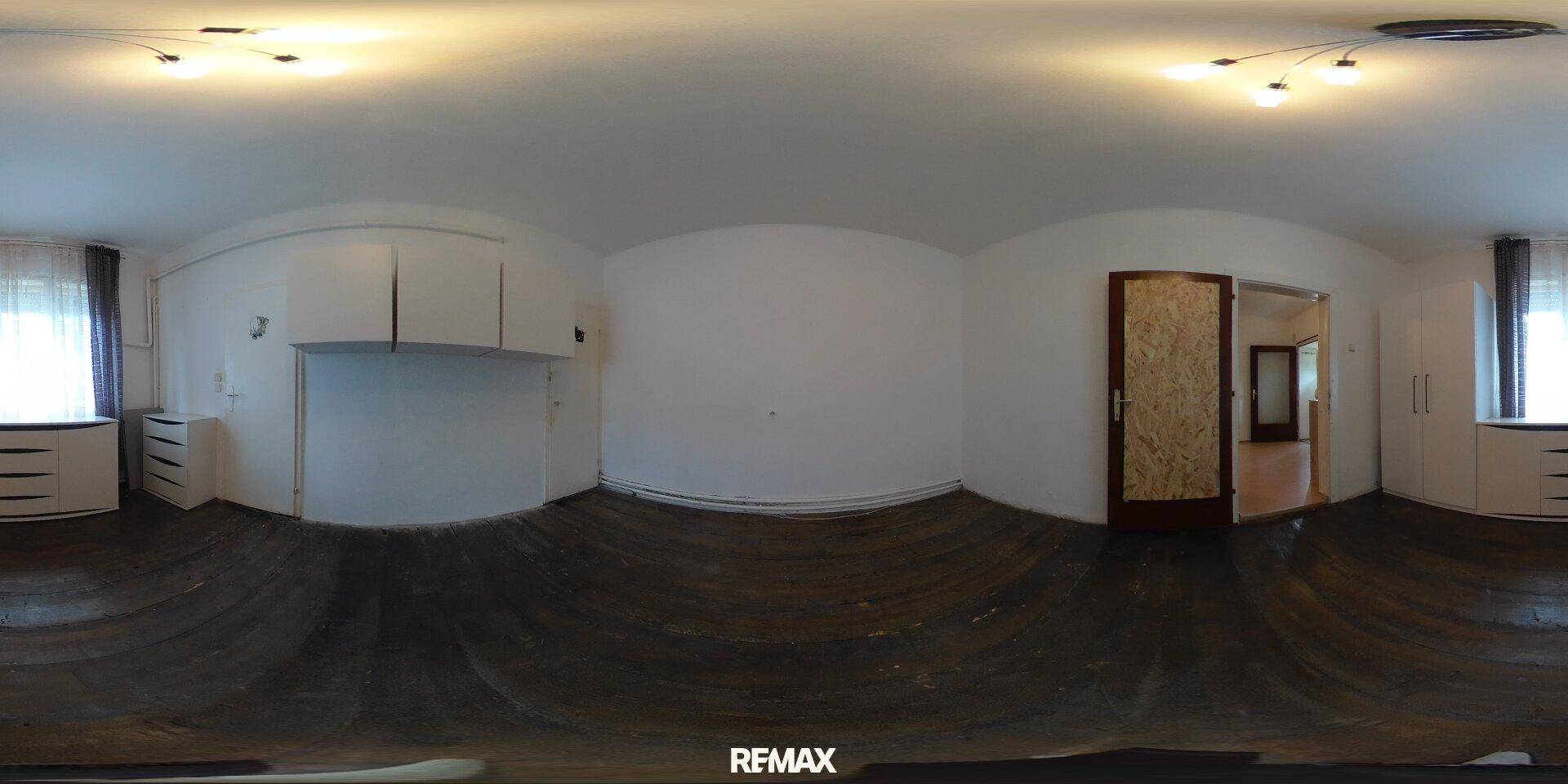 Schlafzimmer mit dunklem Holzboden, weißen Einbauschränken und Fenstern mit Vorhängen.