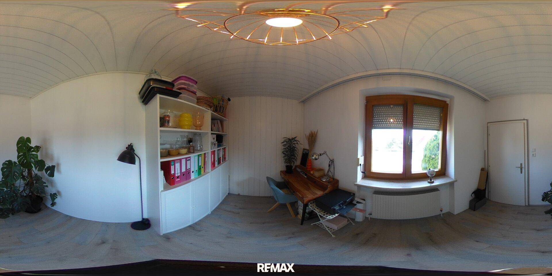 Helles Arbeitszimmer mit Holzvertäfelung, Regal und Schreibtisch am Fenster.