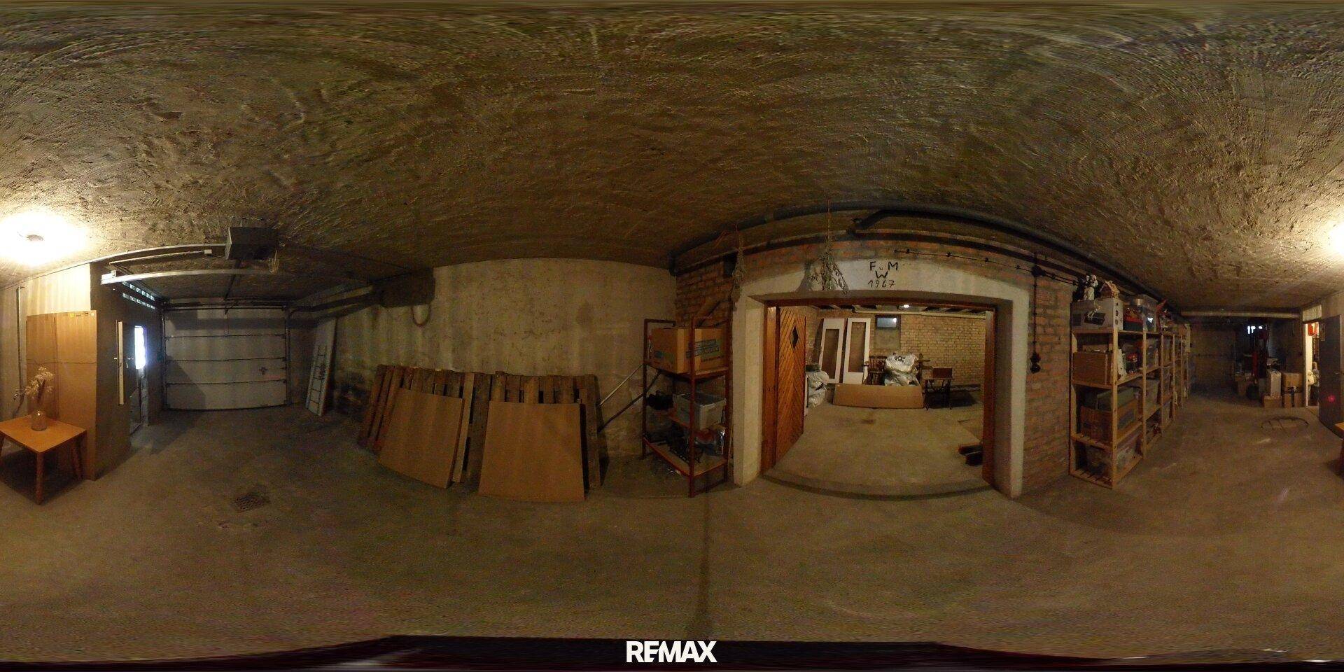 Großer Kellerbereich mit Betonboden, rauen Wänden und einem Garagentor, genutzt als Abstell- und Arbeitsfläche.