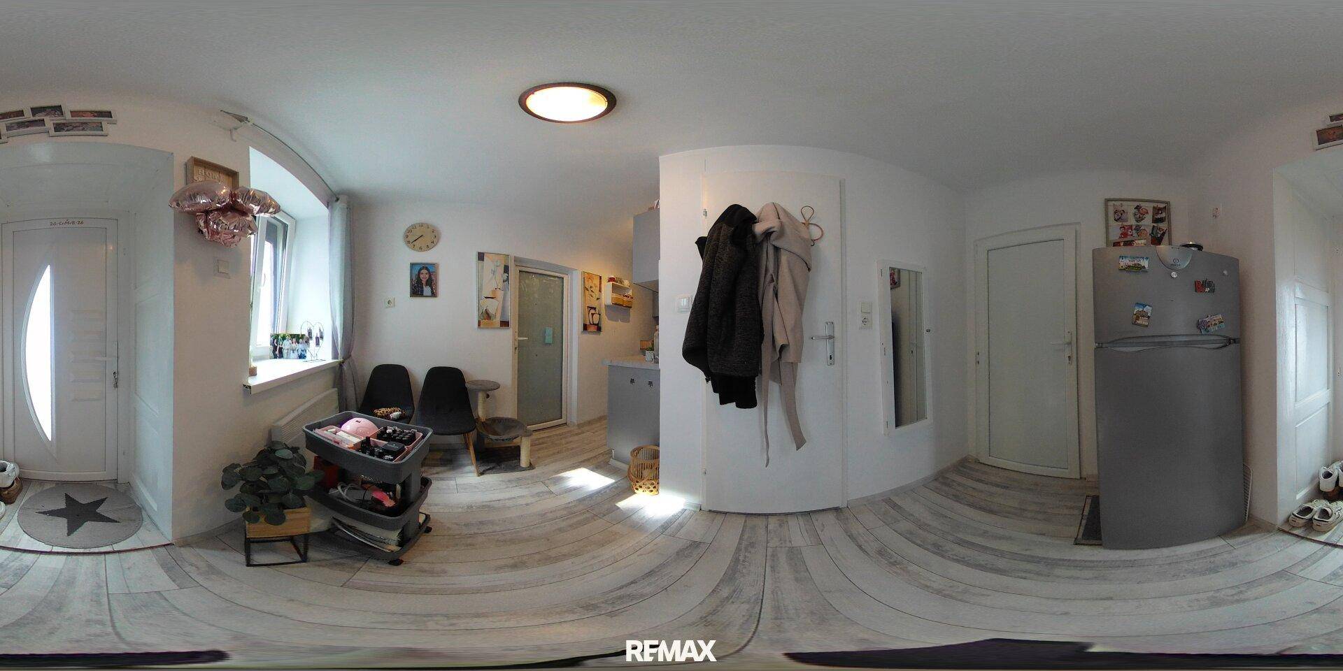 Panoramaansicht des hellen Eingangsbereichs mit Kühlschrank, Fenster und Sitzgelegenheiten.