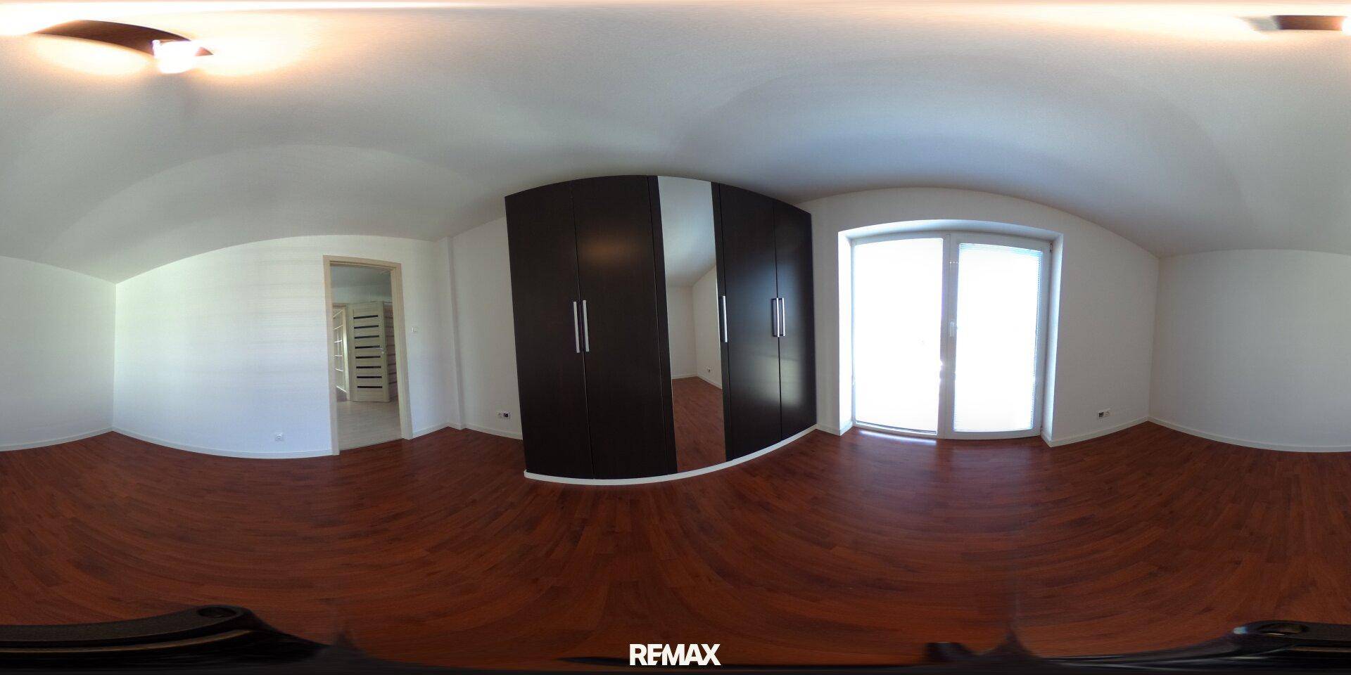 Helles Schlafzimmer mit dunklem Laminatboden, großem Kleiderschrank und Zugang zum Balkon.