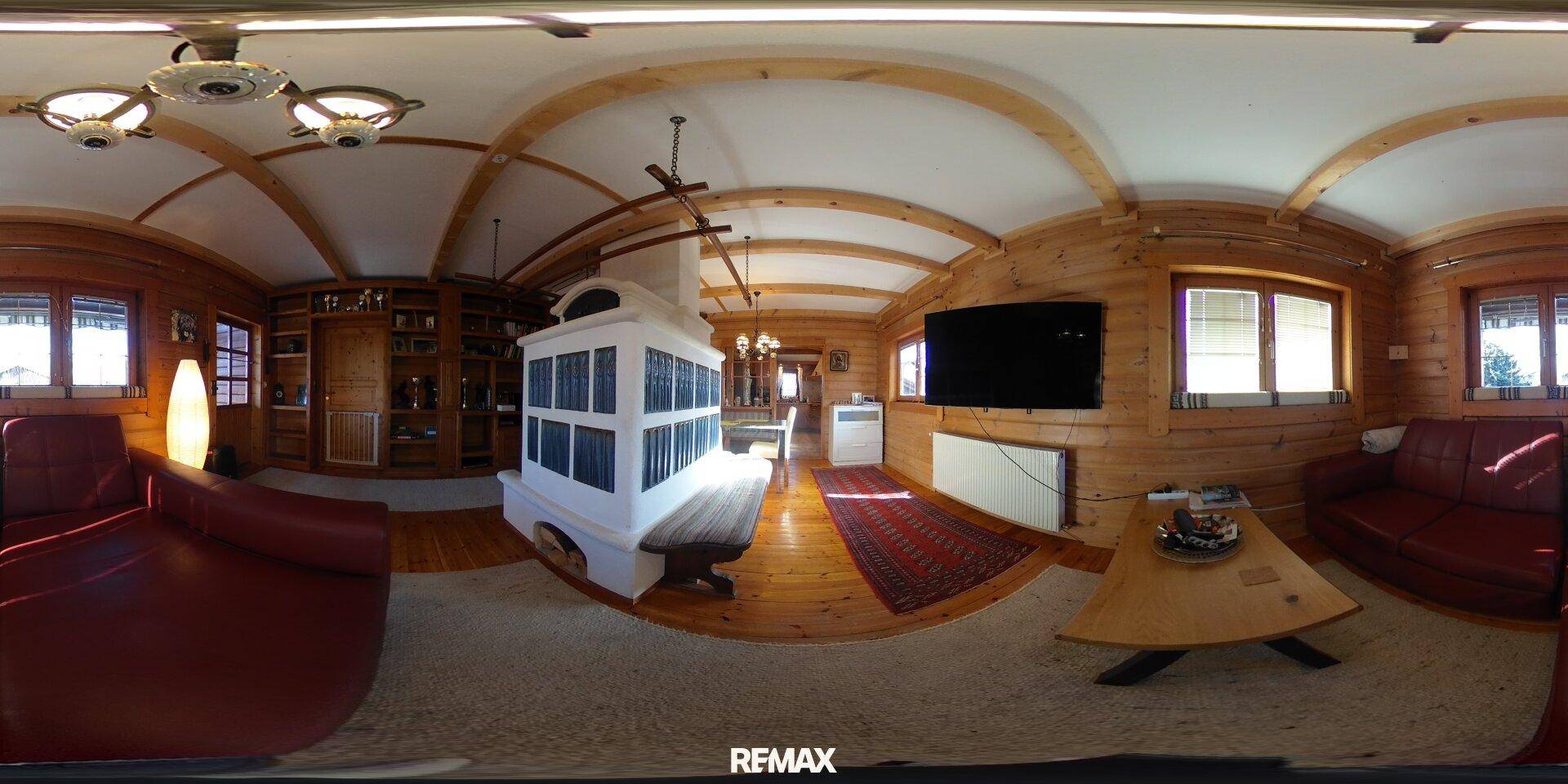 Gemütliches Wohnzimmer mit Holzwänden, Kachelofen und bequemen roten Sofas.