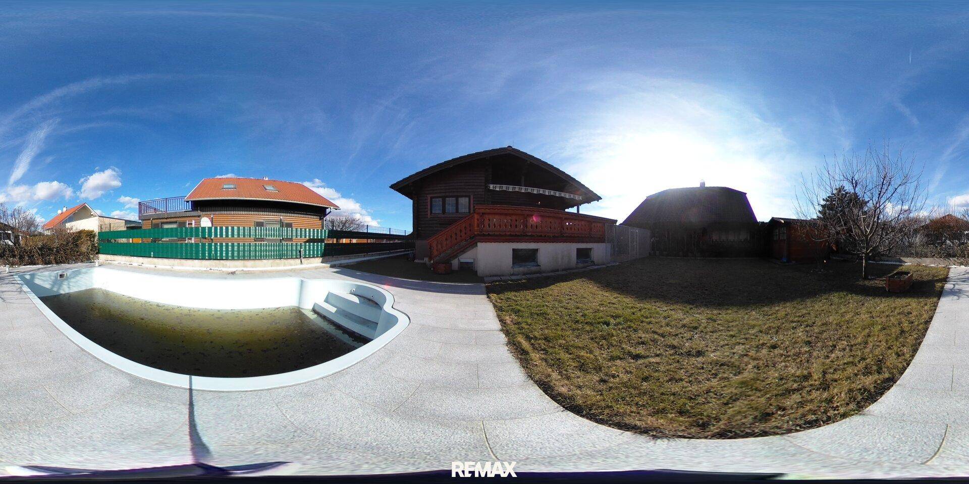 Gartenbereich mit Pool, Rasenfläche und Blick auf das Haus unter blauem Himmel.
