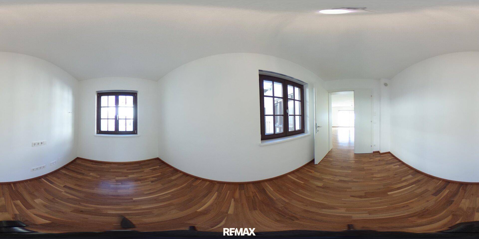 Panoramaaufnahme eines leeren Zimmers mit Parkettboden und zwei Fenstern.