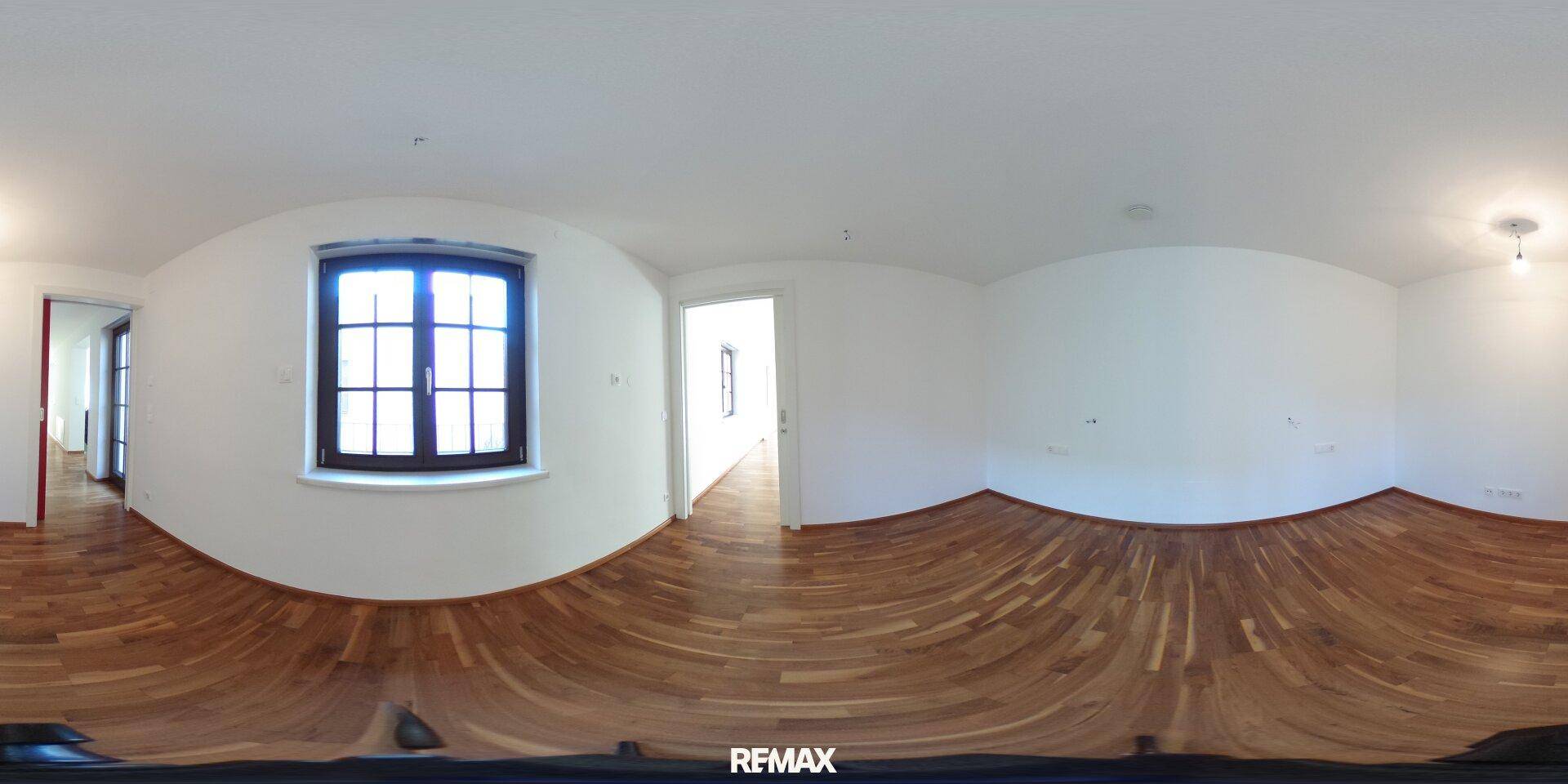 Panoramaaufnahme eines hellen Zimmers mit Parkettboden und Fenster.