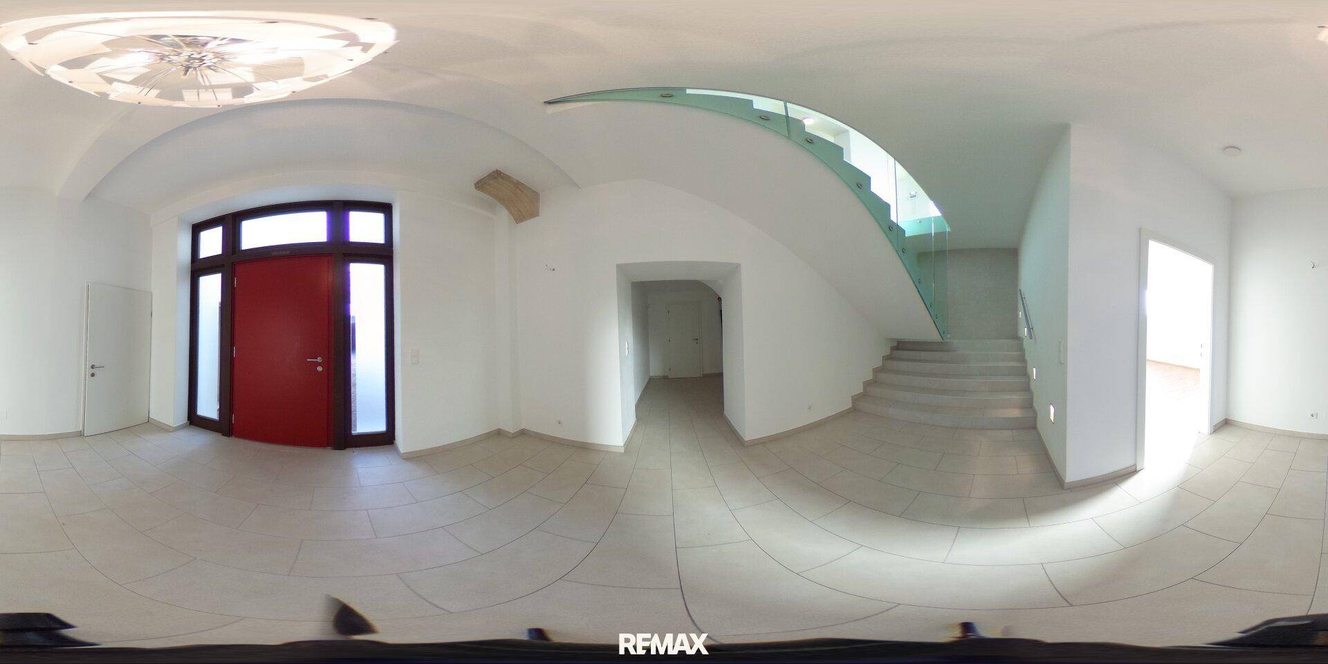 Panoramablick auf einen hellen Eingangsbereich mit moderner Treppe, Fliesenboden und roter Eingangstür.