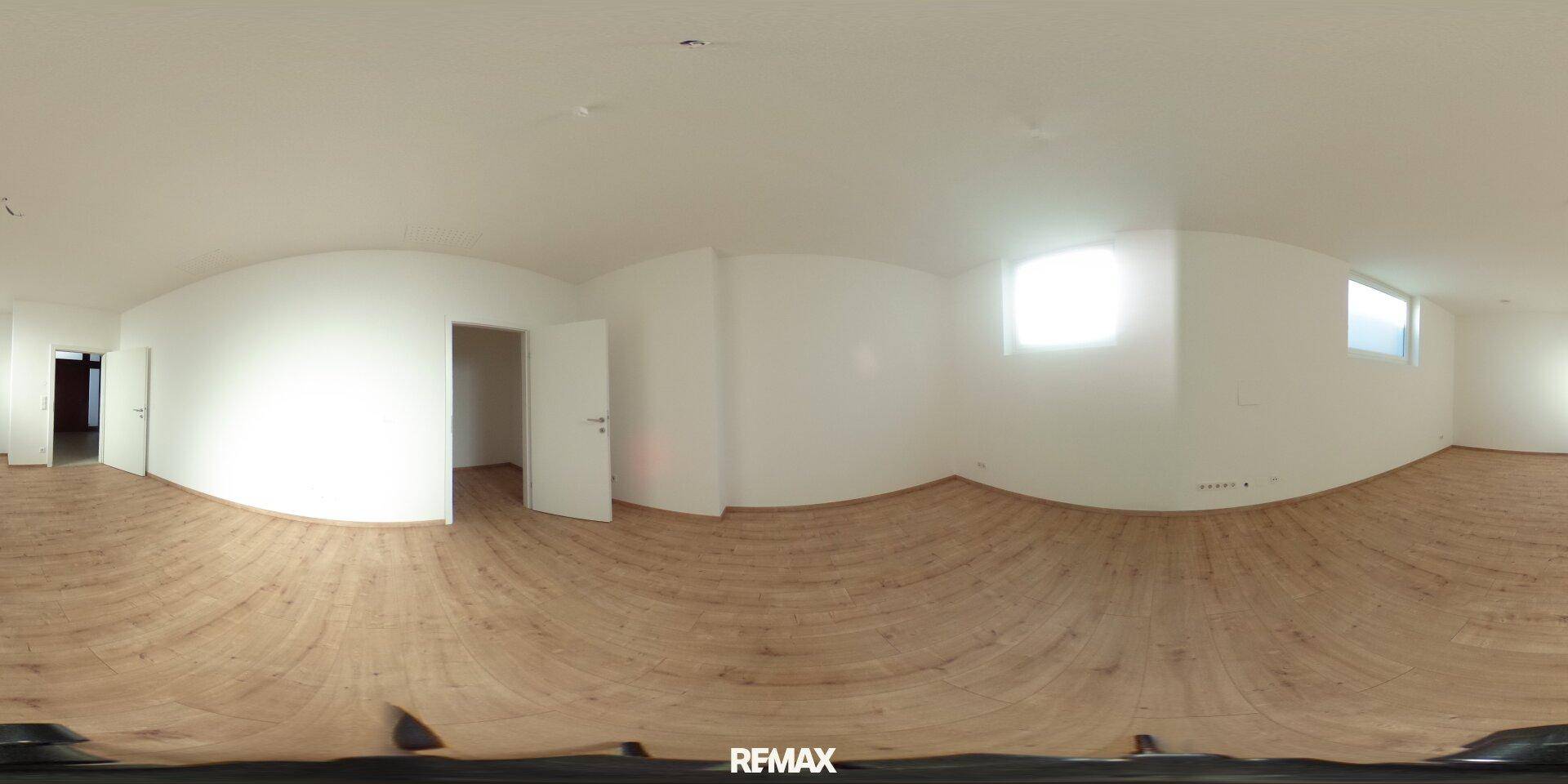 Panoramablick auf einen leeren Raum mit Holzdielenboden und weißen Wänden, der durch mehrere Fenster hell beleuchtet wird.