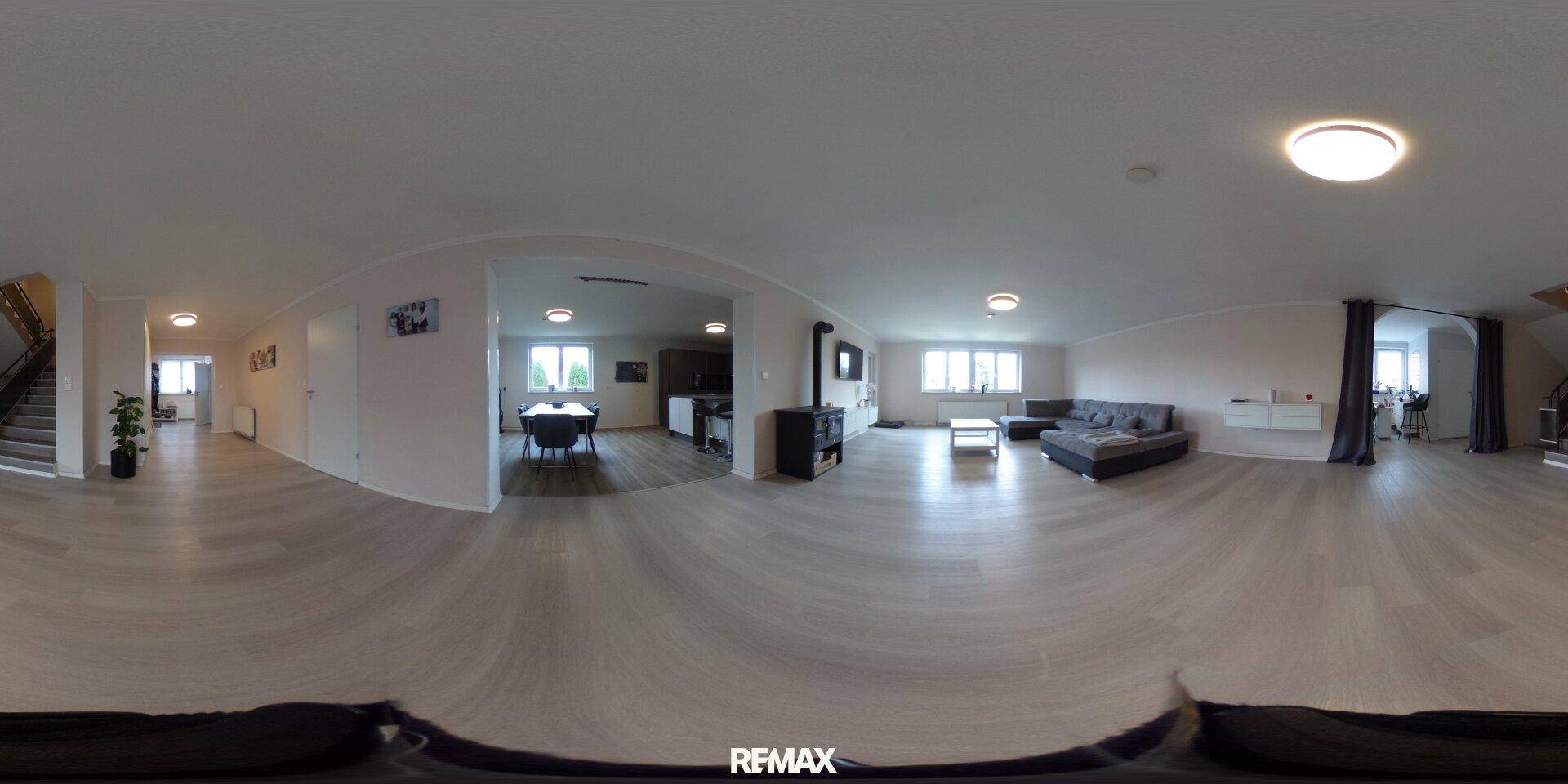 Panoramaaufnahme eines offenen Wohn- und Essbereichs mit hellem Boden und Kaminofen.