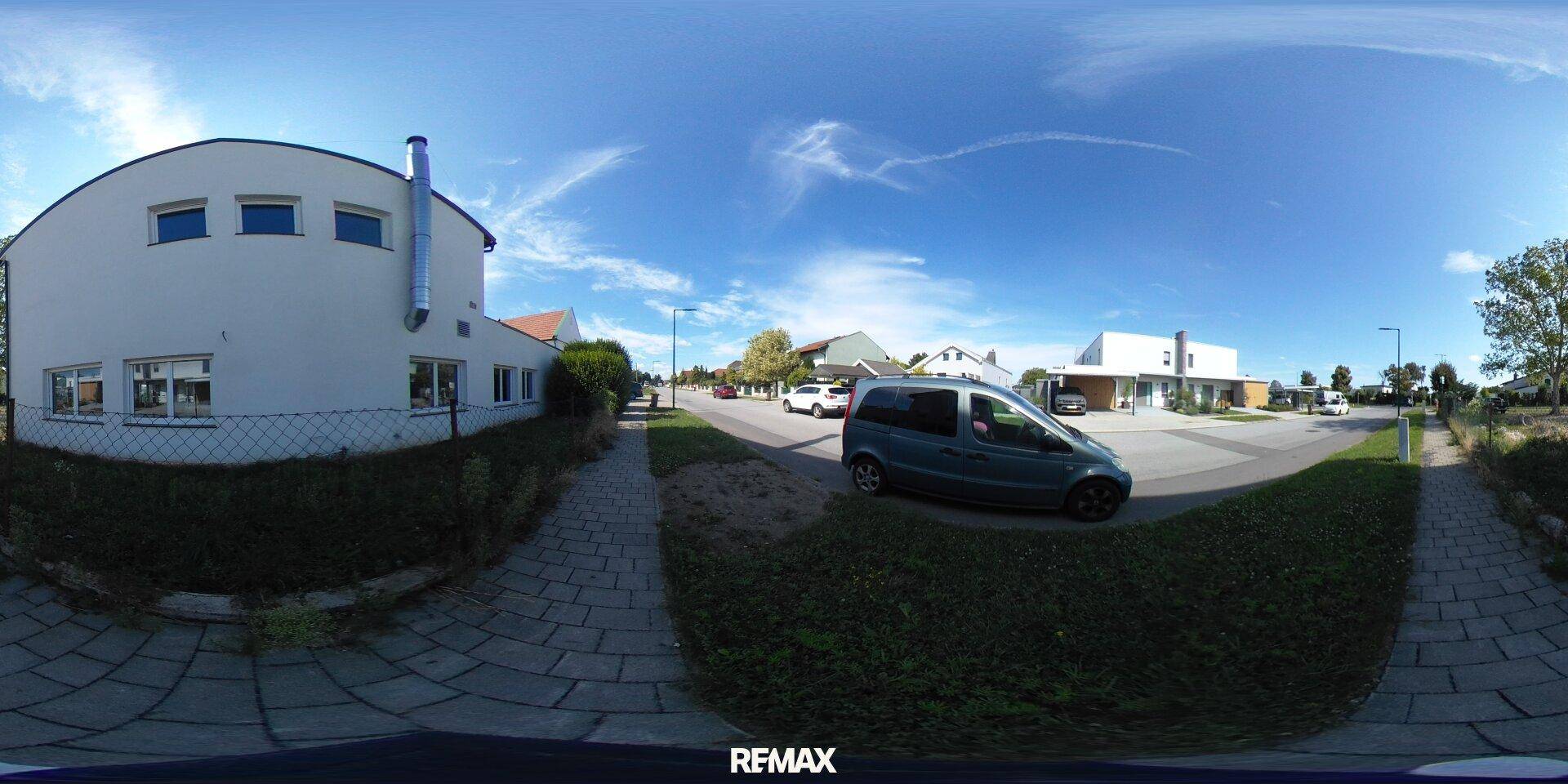 Panoramablick auf ein weißes Gebäude mit blauen Fenstern und die umliegende Wohnstraße.