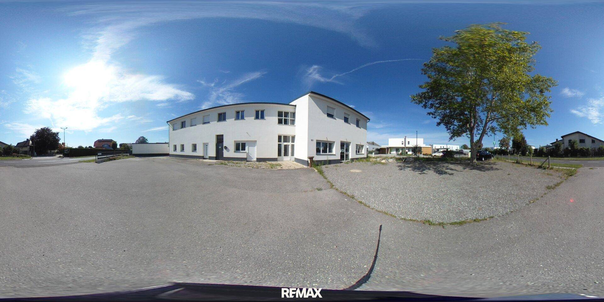 Panoramaansicht des Gebäudes und des umliegenden Geländes unter blauem Himmel.