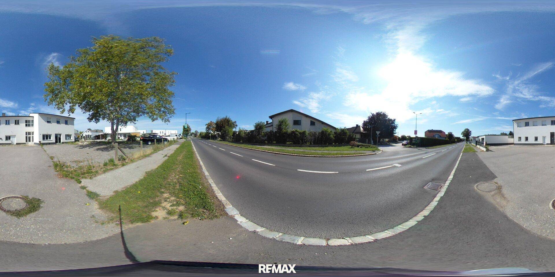 Panoramaansicht der Straße und der Umgebung mit Bäumen und Gebäuden unter strahlendem Himmel.