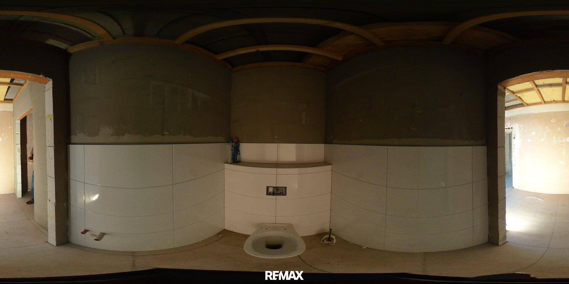 Toilettenraum im Rohbau mit weißen Wandfliesen und einer Wandtoilette, bereit für die Fertigstellung.