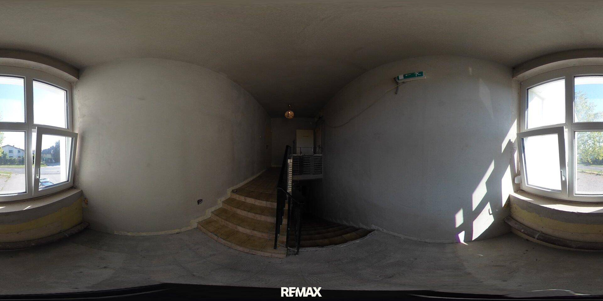 Heller Flur mit großen Fenstern und einer Treppe, die in ein höheres Stockwerk führt.