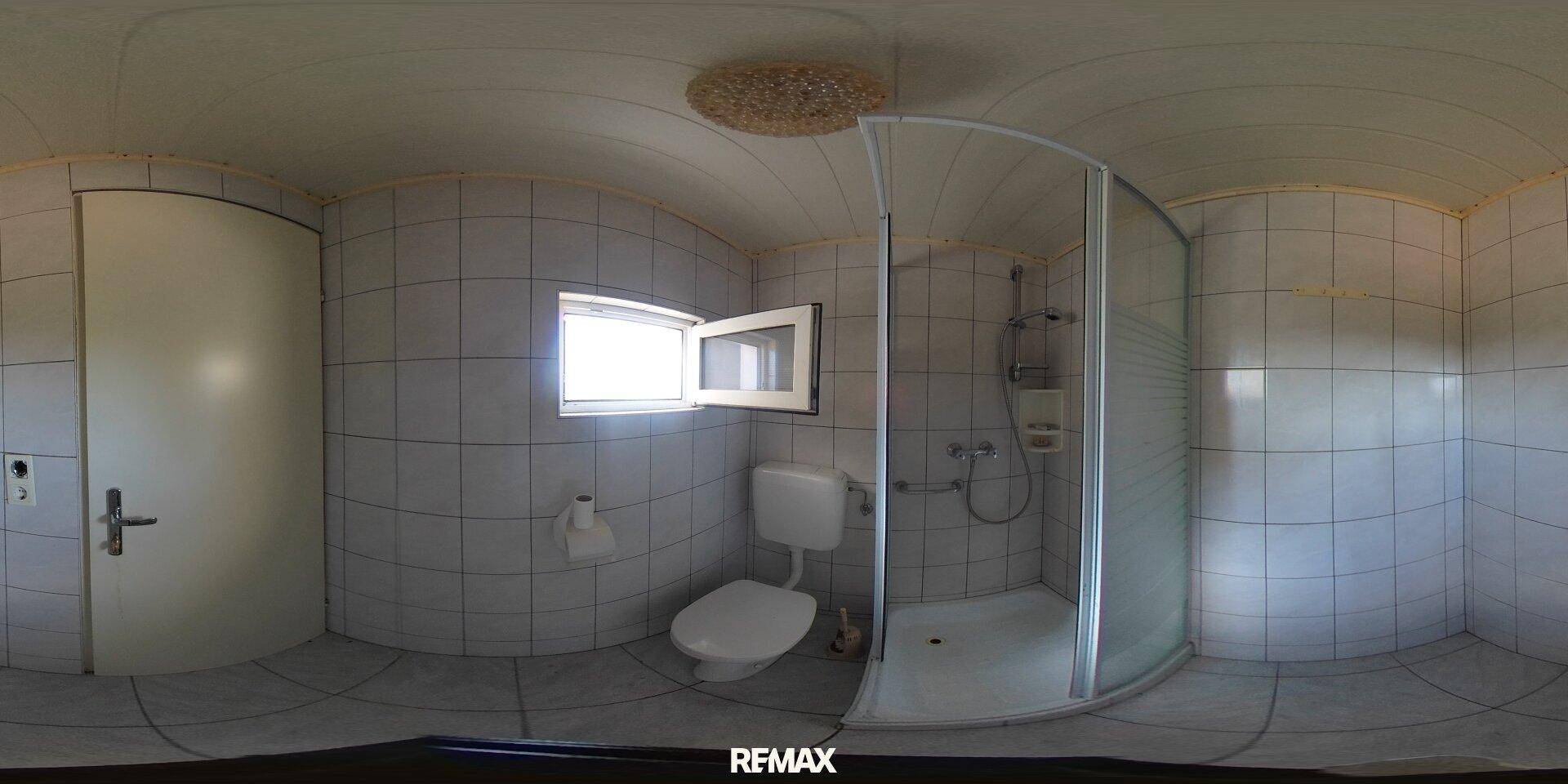 Gefliestes Badezimmer mit Duschkabine, Toilette und Fenster für natürliche Belüftung.