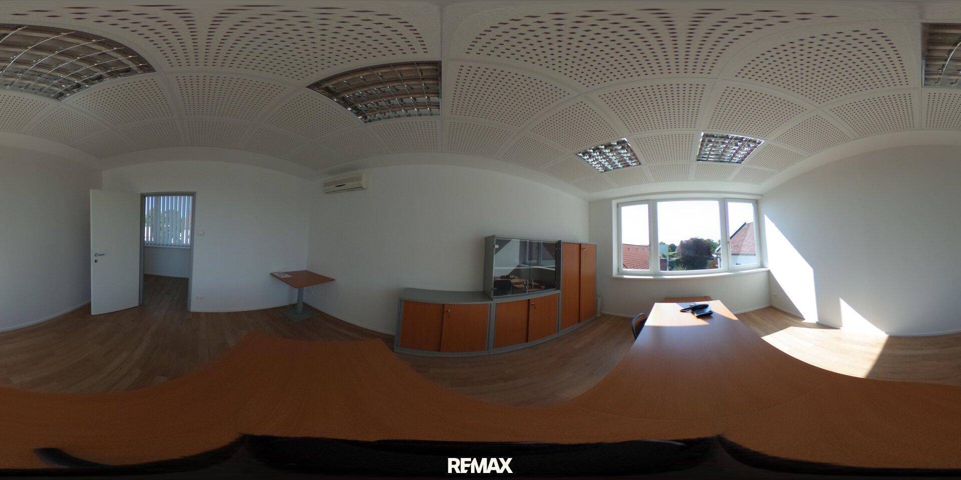 Panoramaansicht eines Büros mit Holzboden, großen Fenstern und integrierten Schränken.