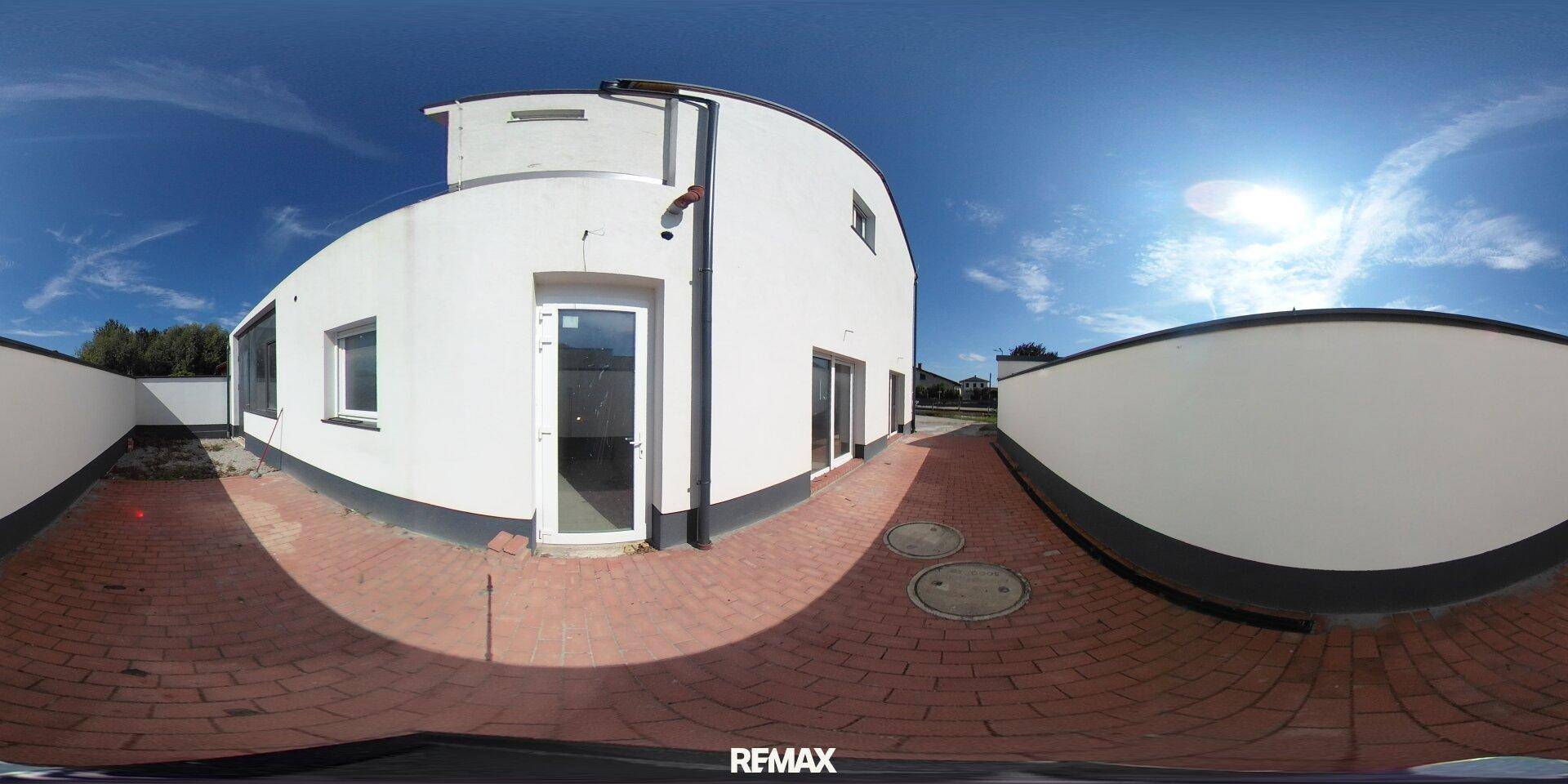 Außenansicht eines Gebäudes mit geschwungener Fassade und gepflastertem Bereich.
