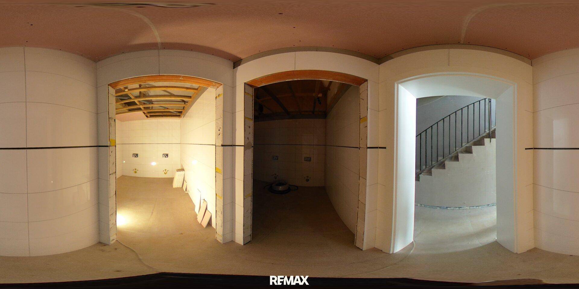 Flur im Rohbau mit mehreren Rundbögen und einer Treppe, die in ein anderes Stockwerk führt.