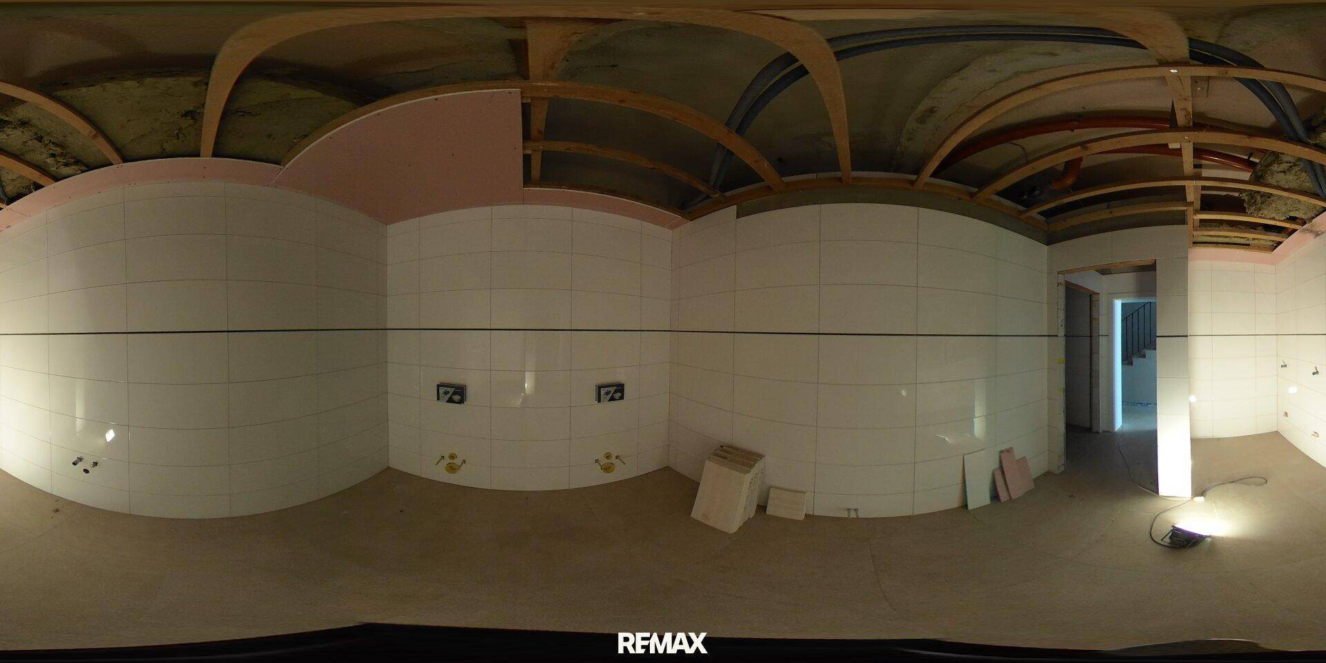 Badezimmer im Rohbau mit weißen Fliesen an den Wänden und sichtbarer Holzkonstruktion an der Decke.