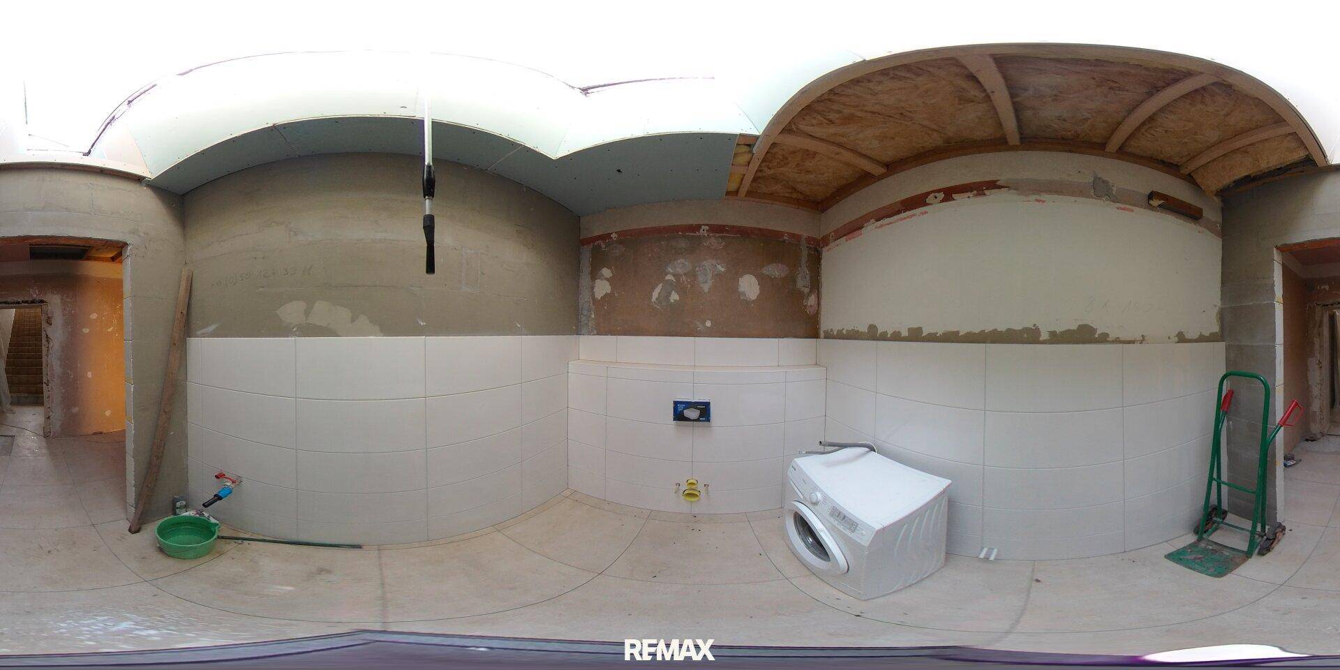 Hauswirtschaftsraum im Rohbau mit gefliesten Wänden und einer Waschmaschine, bereit für den Ausbau.