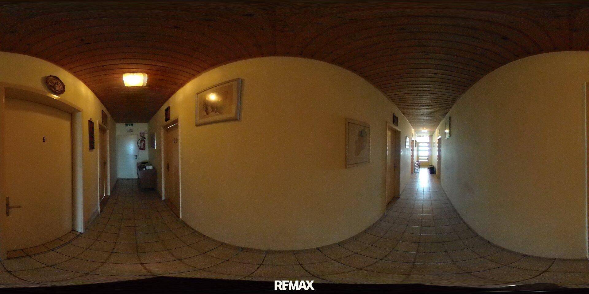 Langer Flur mit Holzdecke und Fliesenboden, der zu verschiedenen Räumen führt.