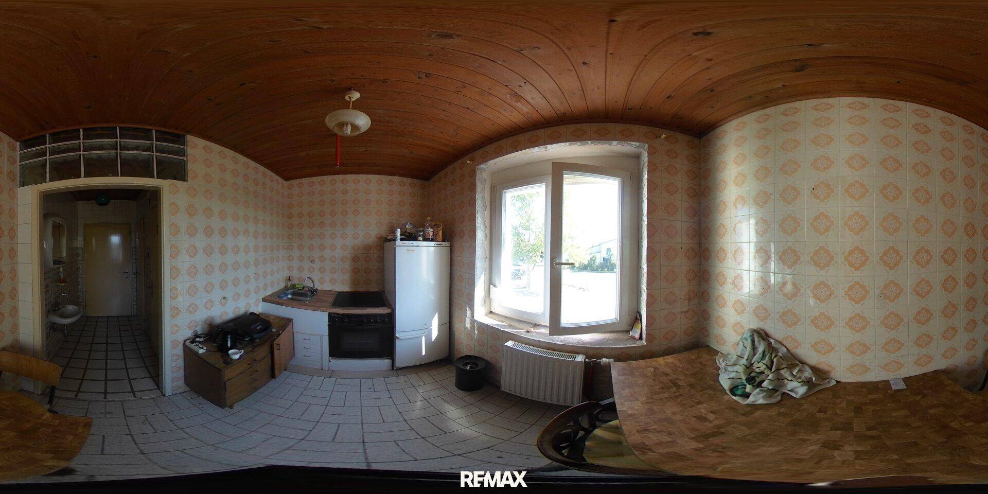 Einfache Küche mit gemusterten Fliesen, Holzdecke und einem Fenster, das Tageslicht hereinlässt.