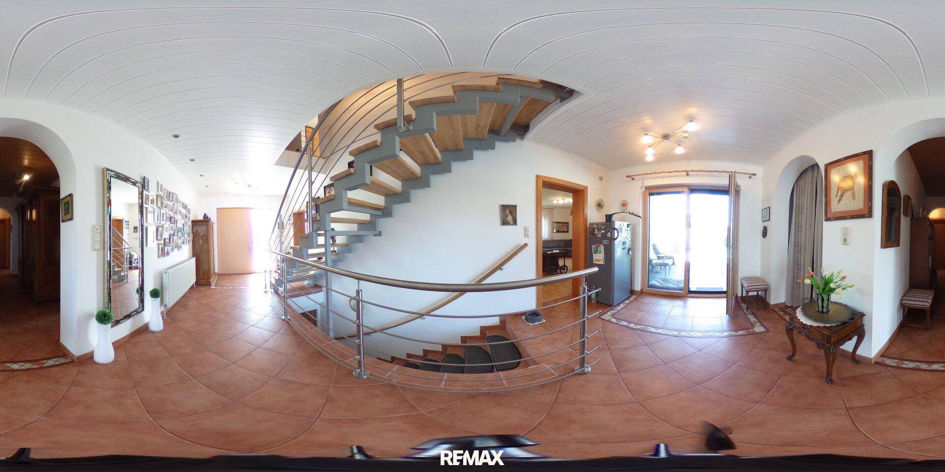 Heller Flur mit geschwungener Treppe, Terrakottafliesen und Zugang zu weiteren Räumen.