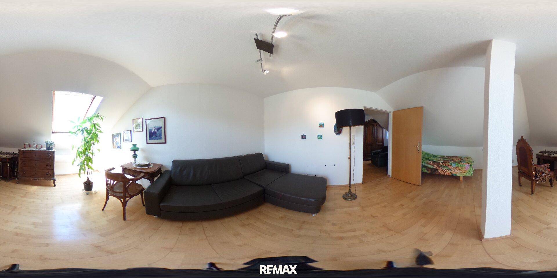Gemütliches Wohnzimmer im Dachgeschoss mit Holzboden, Sofa und Dachschrägen.