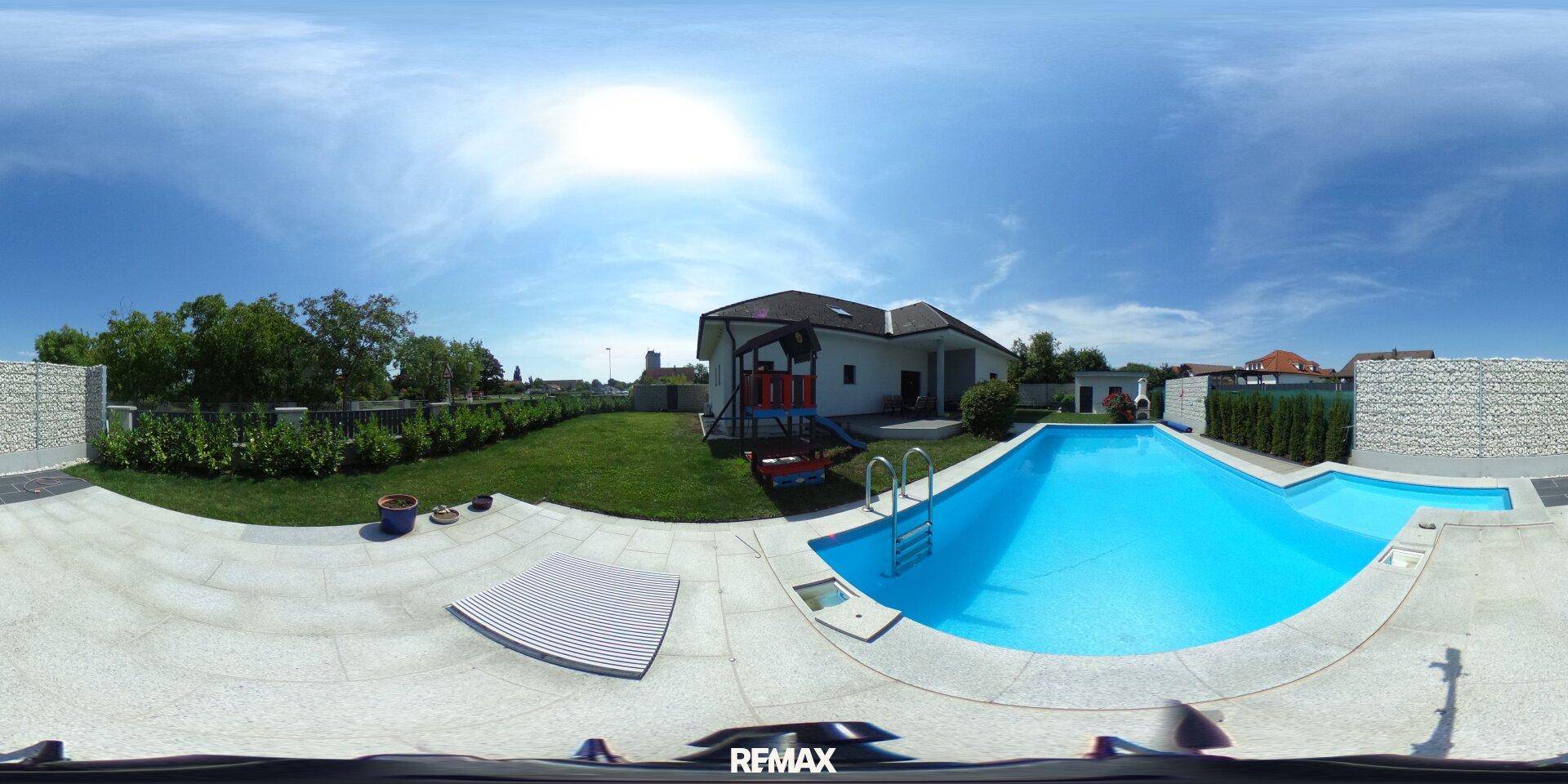 Sonniger Außenbereich mit großem Pool, Terrasse und weitläufiger Rasenfläche.